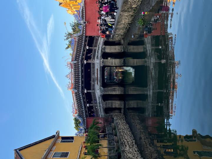 Iconic Japanese Covered Bridge in Hoi An reflecting in the still canal waters under blue skies.