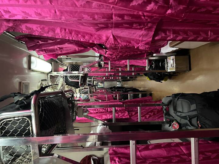 Narrow sleeper train corridor lined with vivid magenta curtains and overhead luggage racks.