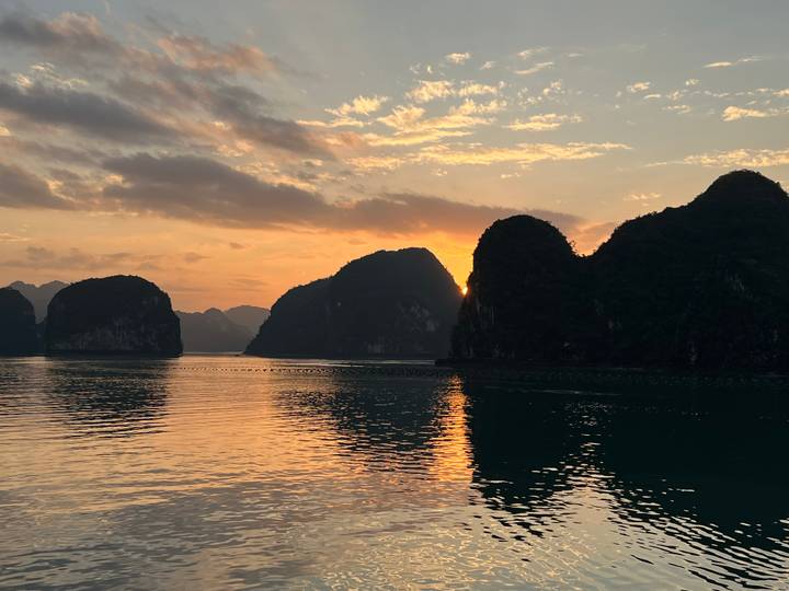 Orange sunset casts warm glow on tranquil waters and towering limestone islands of Ha Long Bay.