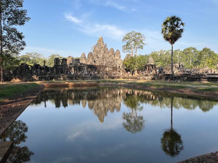 Ancient Bayon temple towers reflected perfectly in a still pond under clear blue sky.