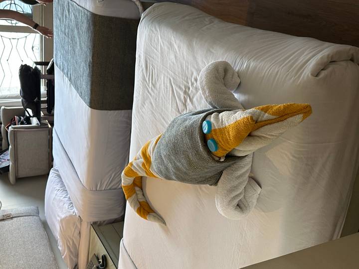 Playful towel sculpture shaped like a crocodile placed on a neatly made cruise cabin bed