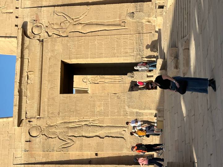 Visitor posing in front of an ancient Egyptian temple wall carved with hieroglyphs