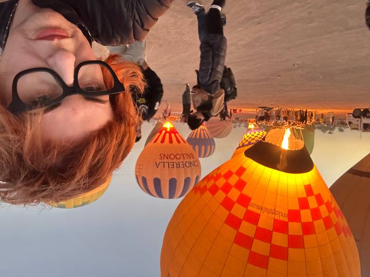 Illuminated hot-air balloons preparing for launch at dawn with a traveller’s selfie in the foreground