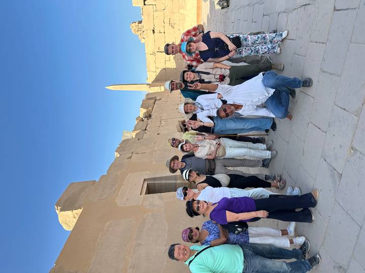 Tour group posing and giving peace signs among ancient temple ruins with an obelisk in the background