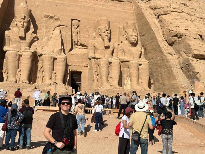 Smiling traveller in front of Abu Simbel’s massive sandstone statues with bustling crowd