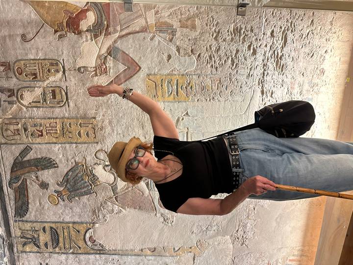 Woman inside tomb pointing at ancient hieroglyphs illuminated by soft interior lighting