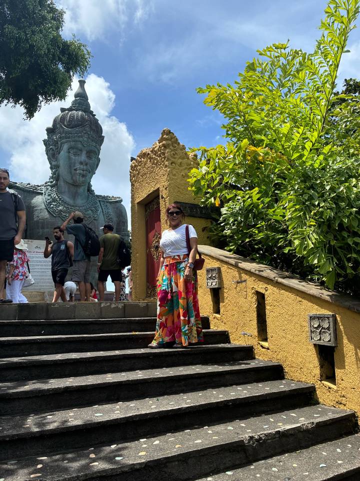 Visitor in colorful skirt posing before the giant Garuda Wisnu Kencana statue with other tourists around.