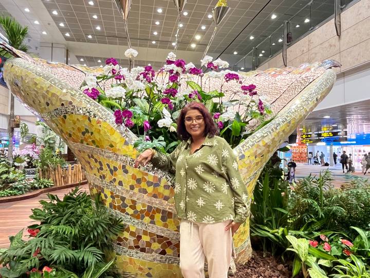 Traveler posing by a huge mosaic floral display inside Singapore Changi Airport terminal.