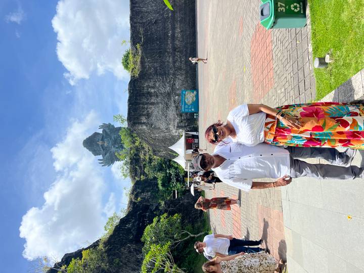 Couple posing under blue sky with the massive Garuda Wisnu Kencana statue rising behind limestone cliffs