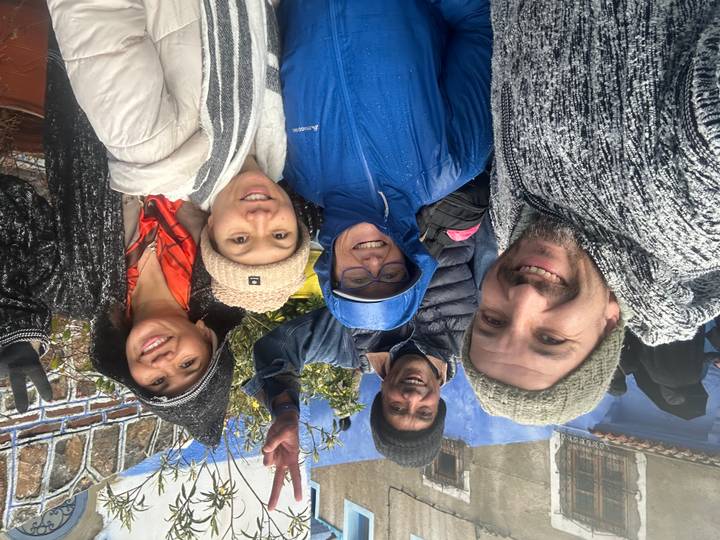 Five tourists in rain gear pose happily against Chefchaouen’s blue-painted walls