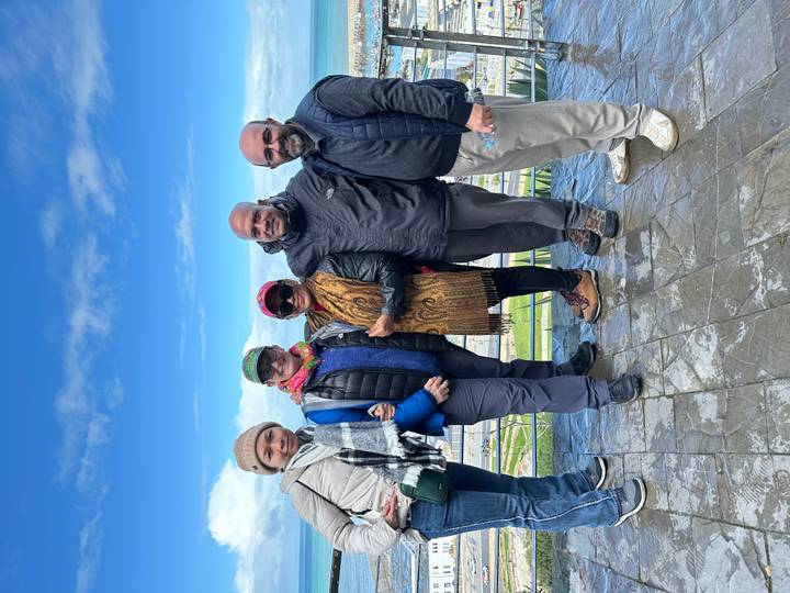 Group of travelers bundled in jackets posing on a lookout platform under a bright blue sky