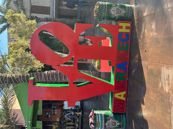 Bright red LOVE Marrakech sculpture framed by palm trees