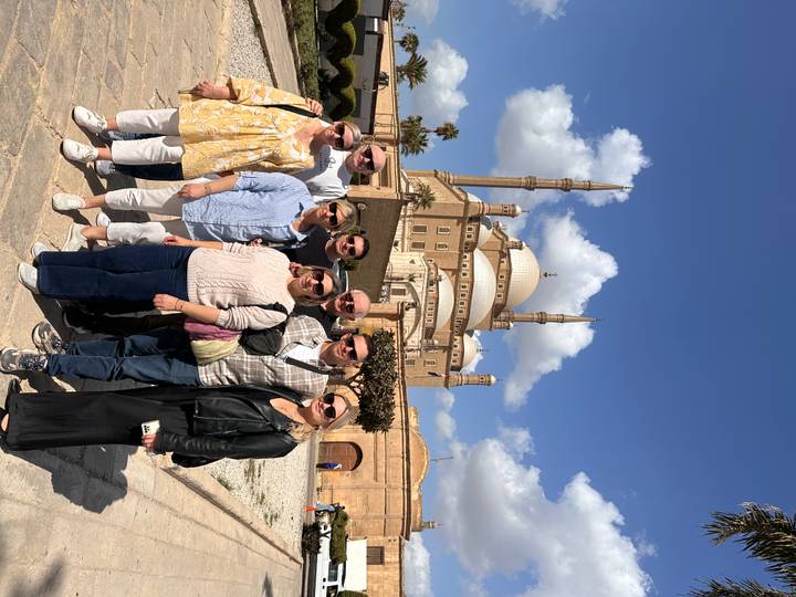 Tour group poses before the grand Muhammad Ali Mosque under a blue sky with fluffy clouds