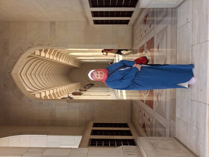 Smiling woman in headscarf poses in arched marble corridor of a grand mosque.