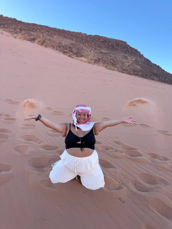 Woman playfully throws handfuls of pink desert sand into the air leaving arcs around her.