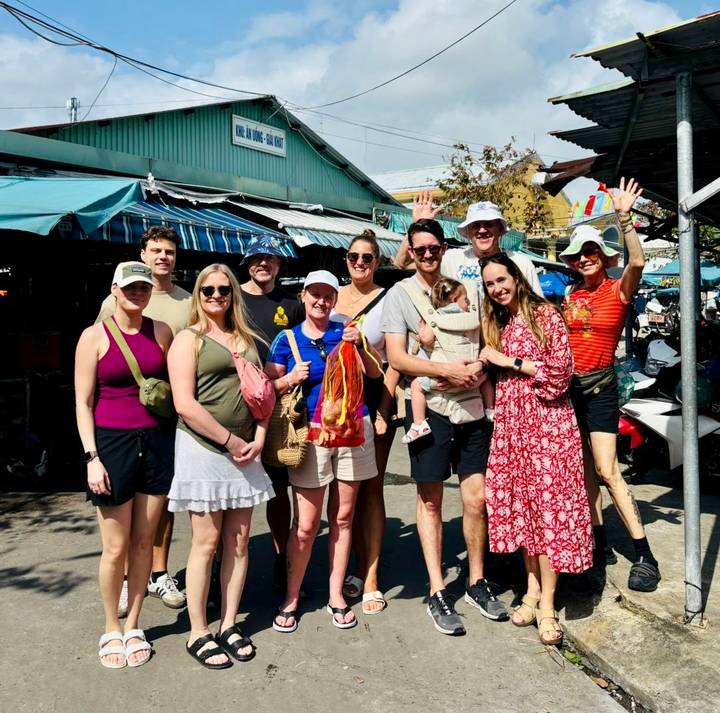 Happy travel group posing at an outdoor Vietnamese market under bright sunlight