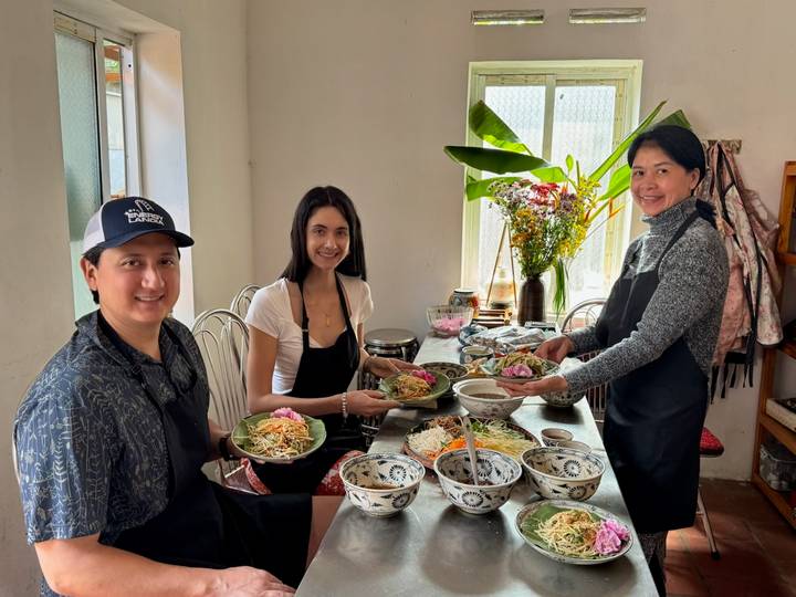 Small cooking class holding plates of prepared Vietnamese dishes in a bright kitchen.