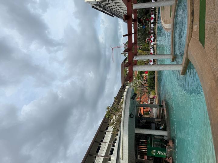Resort swimming pool surrounded by buildings under a cloudy sky.
