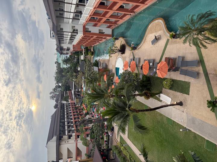 Elevated sunset view of a large resort with pools, palm trees and loungers.