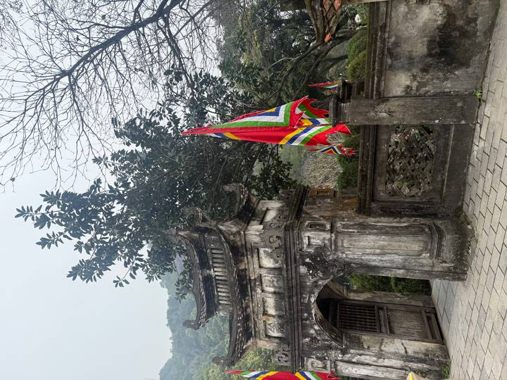 Old stone gate with colorful flags and bare tree branches on a grey day.