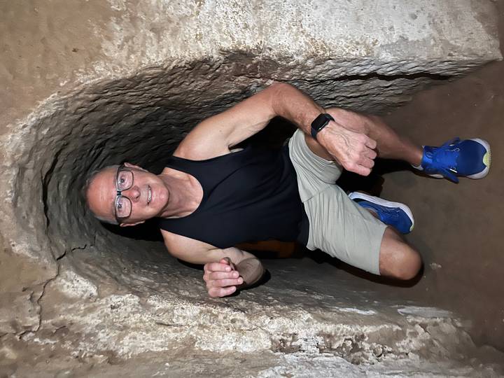 Man kneels inside a narrow earthen tunnel, showcasing the cramped Cu Chi passageways.
