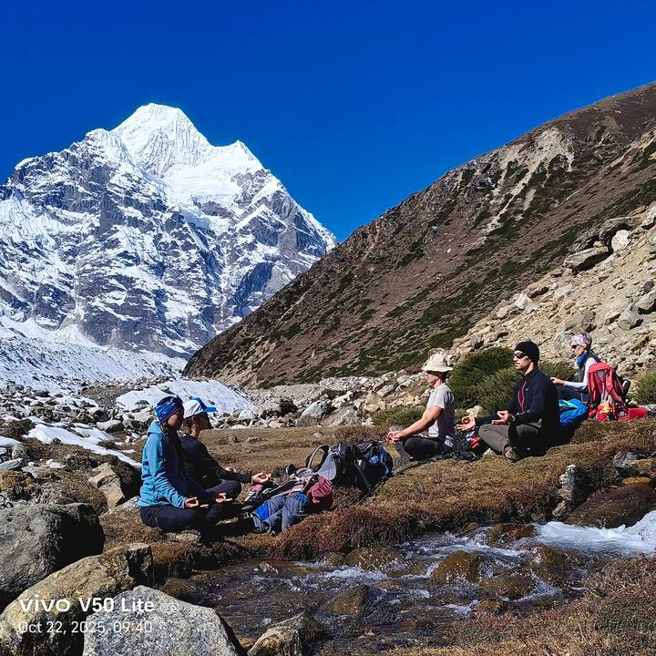 Small group meditates on grassy ground with a massive snowy peak towering behind.