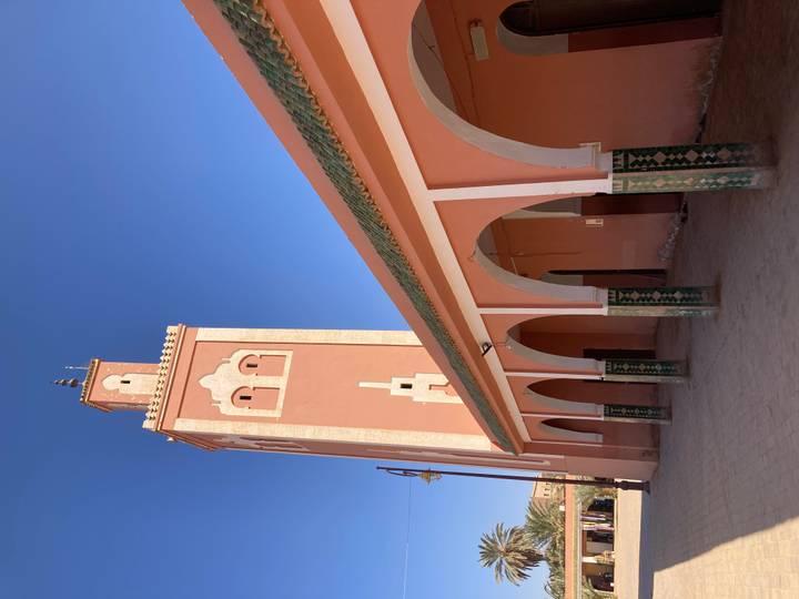 Tall pink minaret and arched veranda of a village mosque set against deep blue sky.