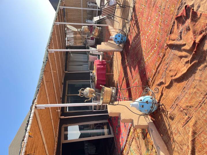 Outdoor dining terrace with rugs, teapots and desert camp structures under bright sky.