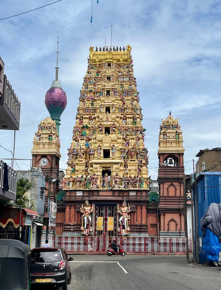 Vibrant Hindu temple gopuram covered in colorful statues with Colombo Lotus Tower in background.