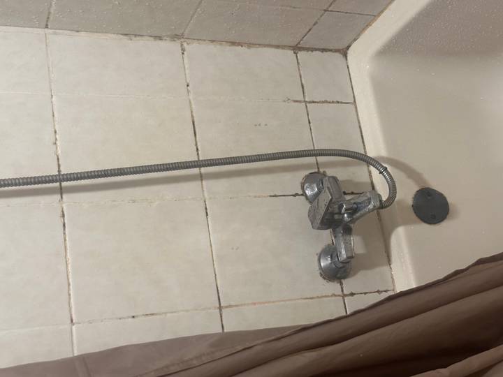 A worn bathtub and shower fixture with stained tiles and a dangling metal hose