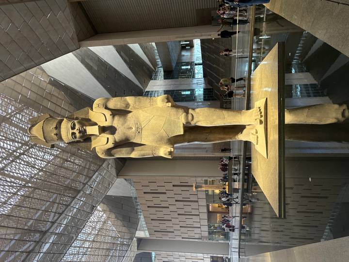 Massive statue of pharaoh within the Grand Egyptian Museum atrium reflected in a water feature.