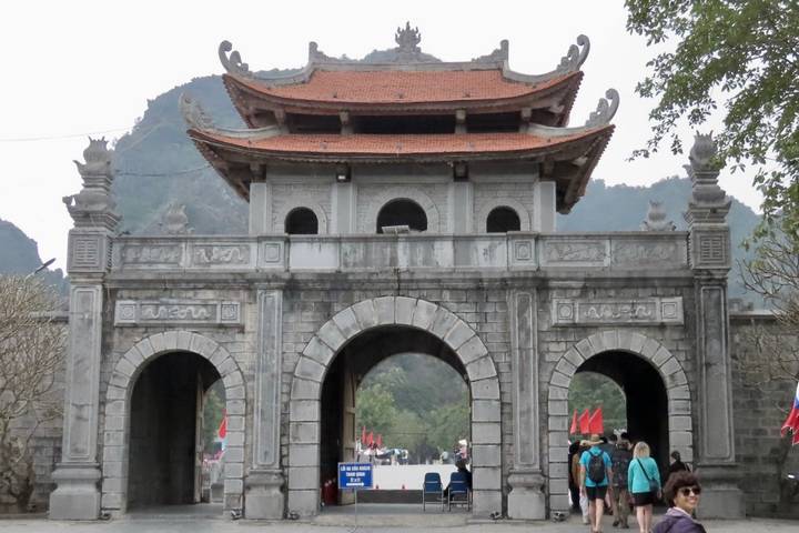 Stone entrance gate with three arches set against limestone peaks, visitors walking below.