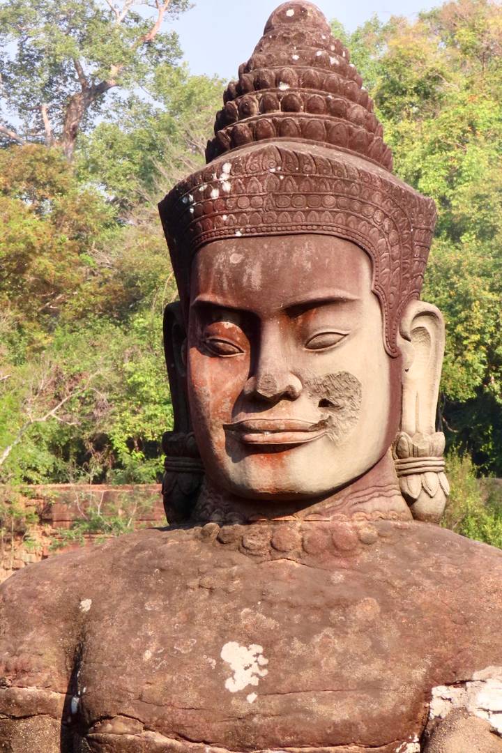 Close-up stone face carving from an ancient Khmer temple framed by greenery.