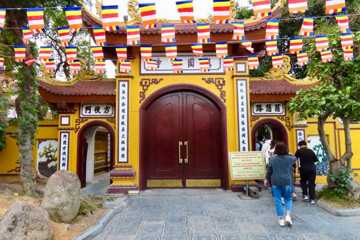 Bright yellow temple entrance with red double doors and strings of colorful flags overhead.