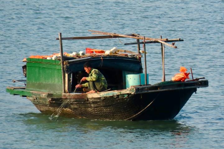 Small green fishing boat on open water with a fisherman working aboard.