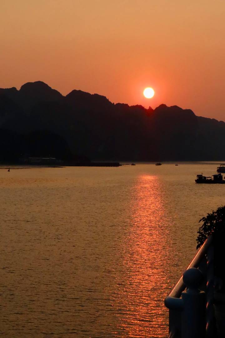 Glowing orange sunset reflecting across a wide bay bordered by dark silhouettes of hills.