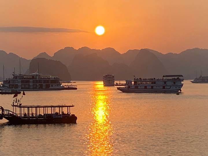 Golden sun sets over limestone karsts and cruise boats in Halong Bay, Vietnam.