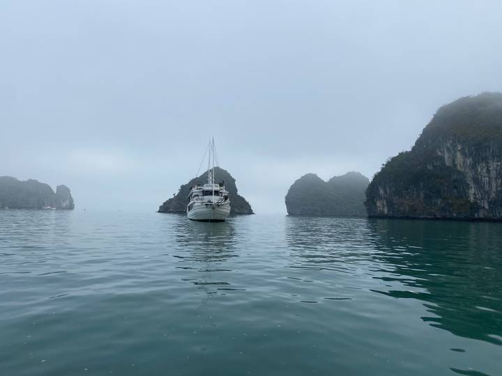 Single cruise boat anchored among mist-shrouded limestone islands on a calm bay.