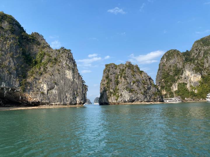 Turquoise waters between towering limestone cliffs under clear sky in Halong Bay.