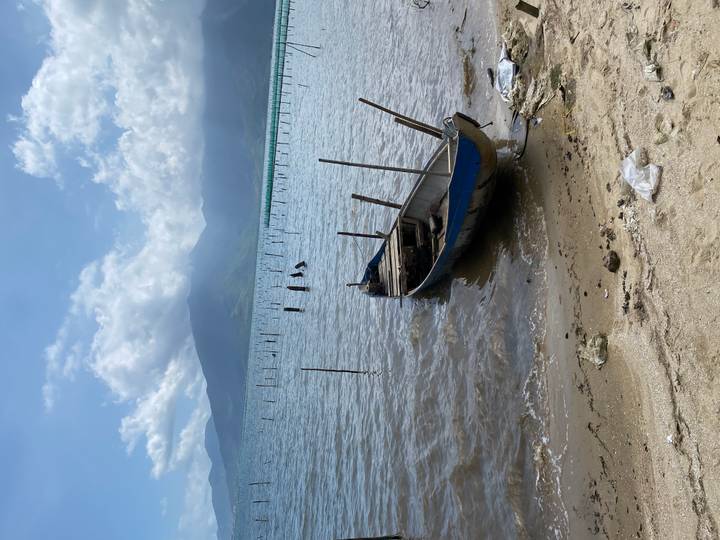 Weathered wooden boat rests on tranquil lagoon shore with misty mountains beyond.
