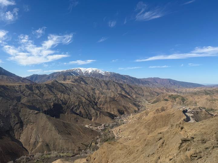 Snow-tipped High Atlas Mountains rise above rugged valleys and winding mountain road.