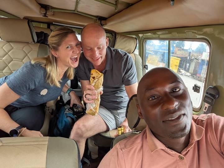 Three cheerful travelers inside a safari jeep, joking around while holding a rolled snack.