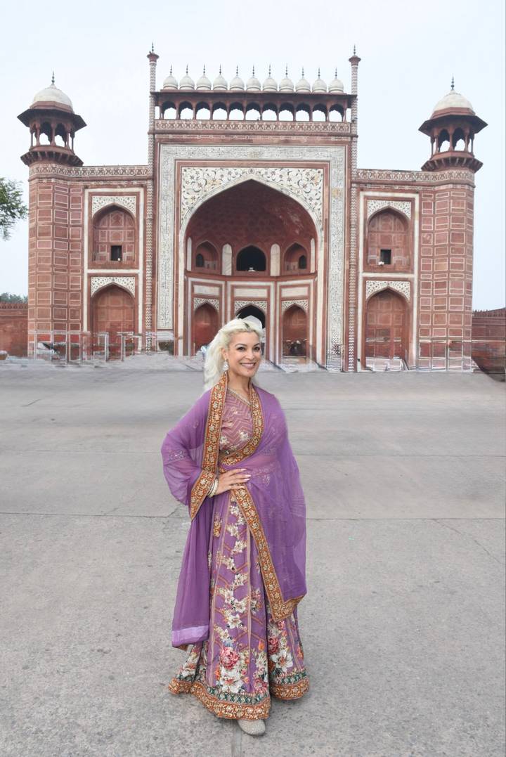 Smiling woman in purple traditional dress poses before ornate Mughal gateway