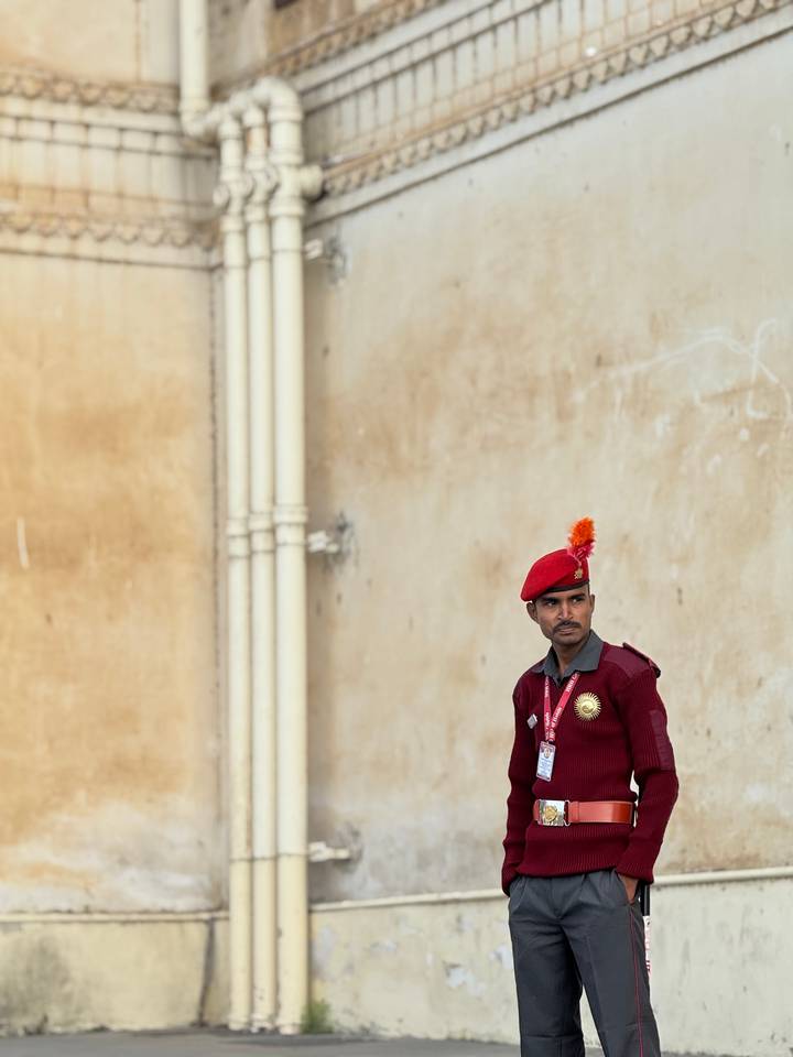 Uniformed guard in red beret standing against a textured ochre wall