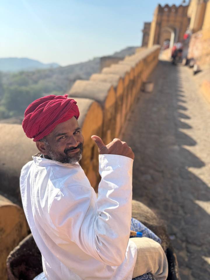 Local man in bright red turban giving a thumbs-up along a sunlit fort rampart