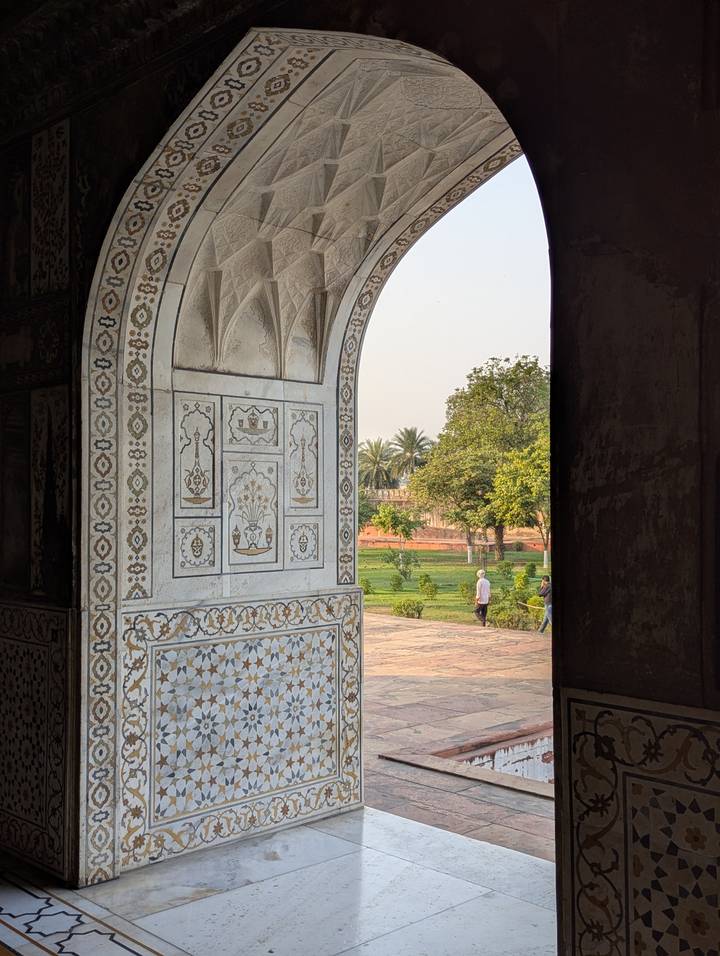Decorative marble-inlaid archway framing a sunny garden with a lone visitor strolling on a path