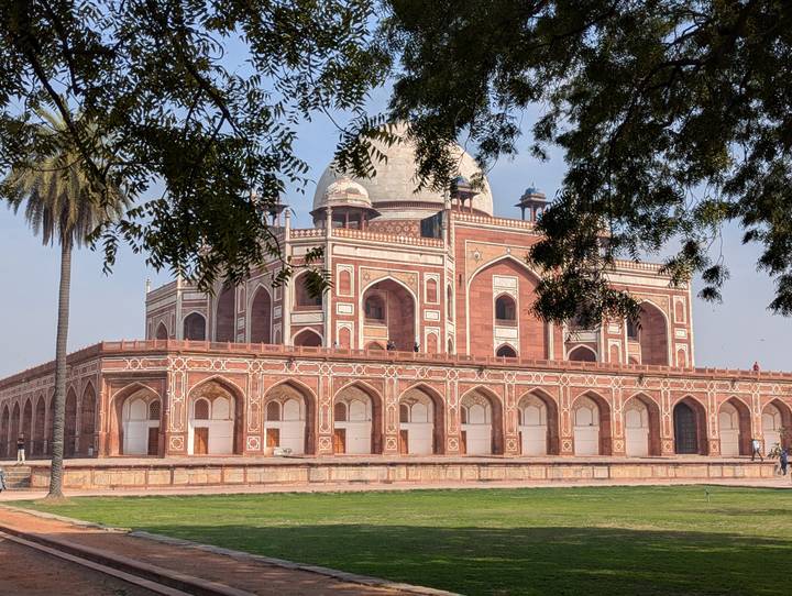 Red-sandstone Humayun’s Tomb framed by leafy branches on a clear morning