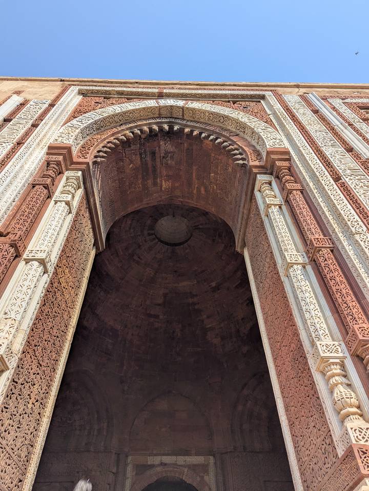 Detailed view of carved red and white sandstone arch leading into a vast dome