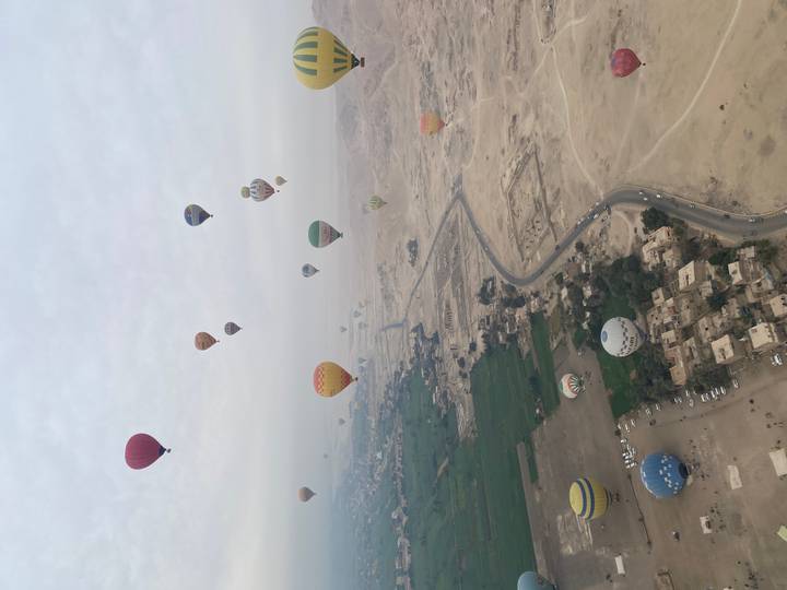 Dozens of colorful hot-air balloons floating above a patchwork of green fields and desert near the Nile.