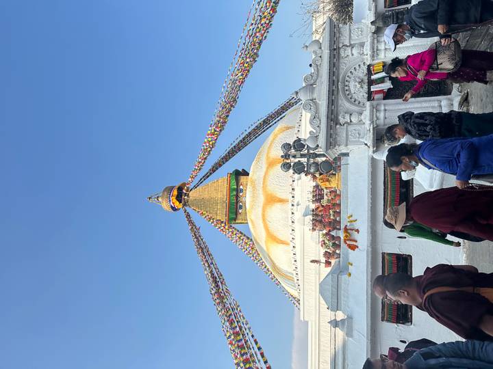 Boudhanath Stupa draped with colorful prayer flags against a clear blue sky.